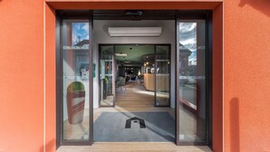 L’entrée d’un hôtel, avec des portes en verre, un comptoir d’accueil et un espace salon visible à l’intérieur.