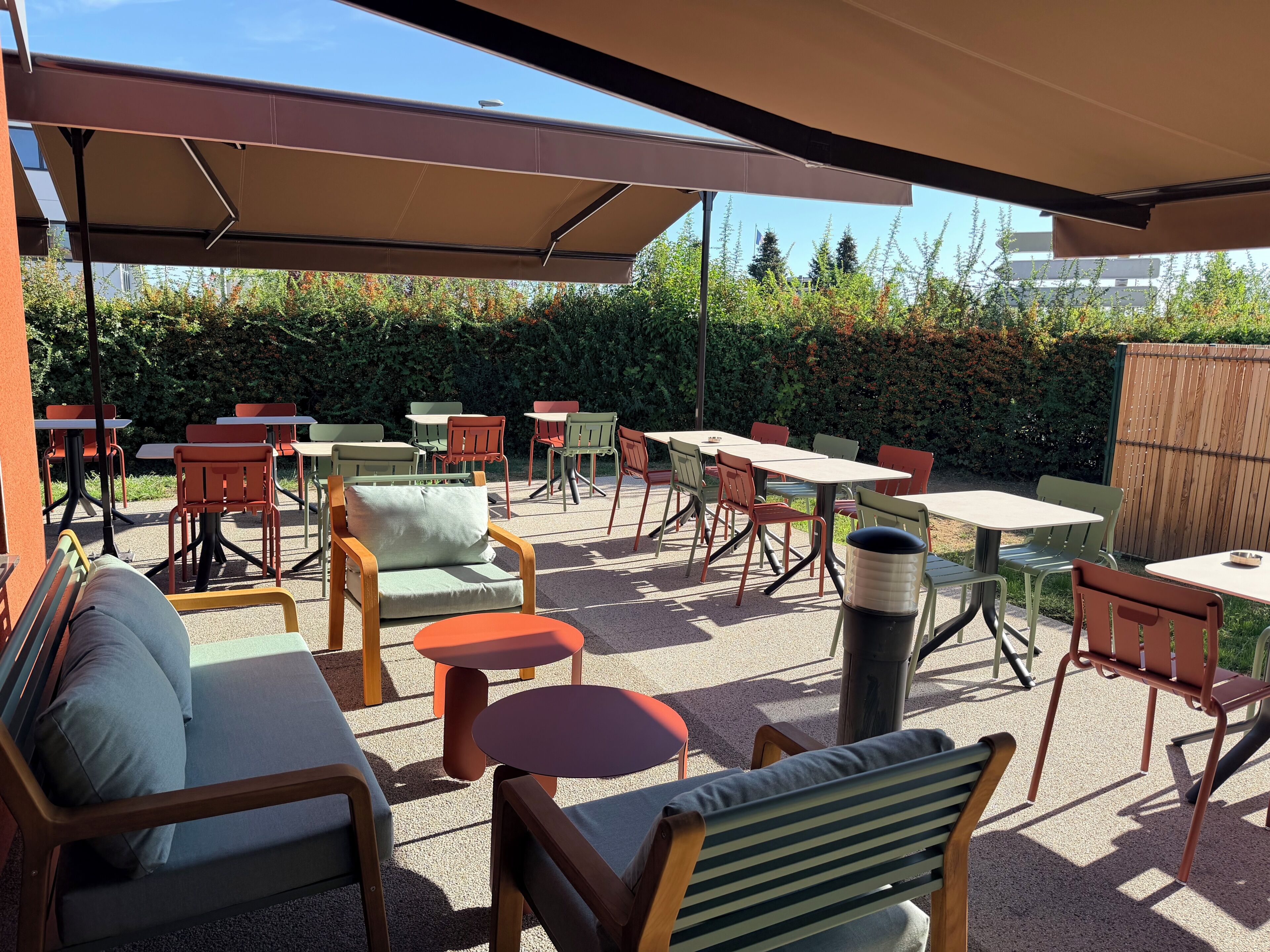 Un área de patio al aire libre con varias mesas y sillas, un bote de basura y una zona de estar cubierta.