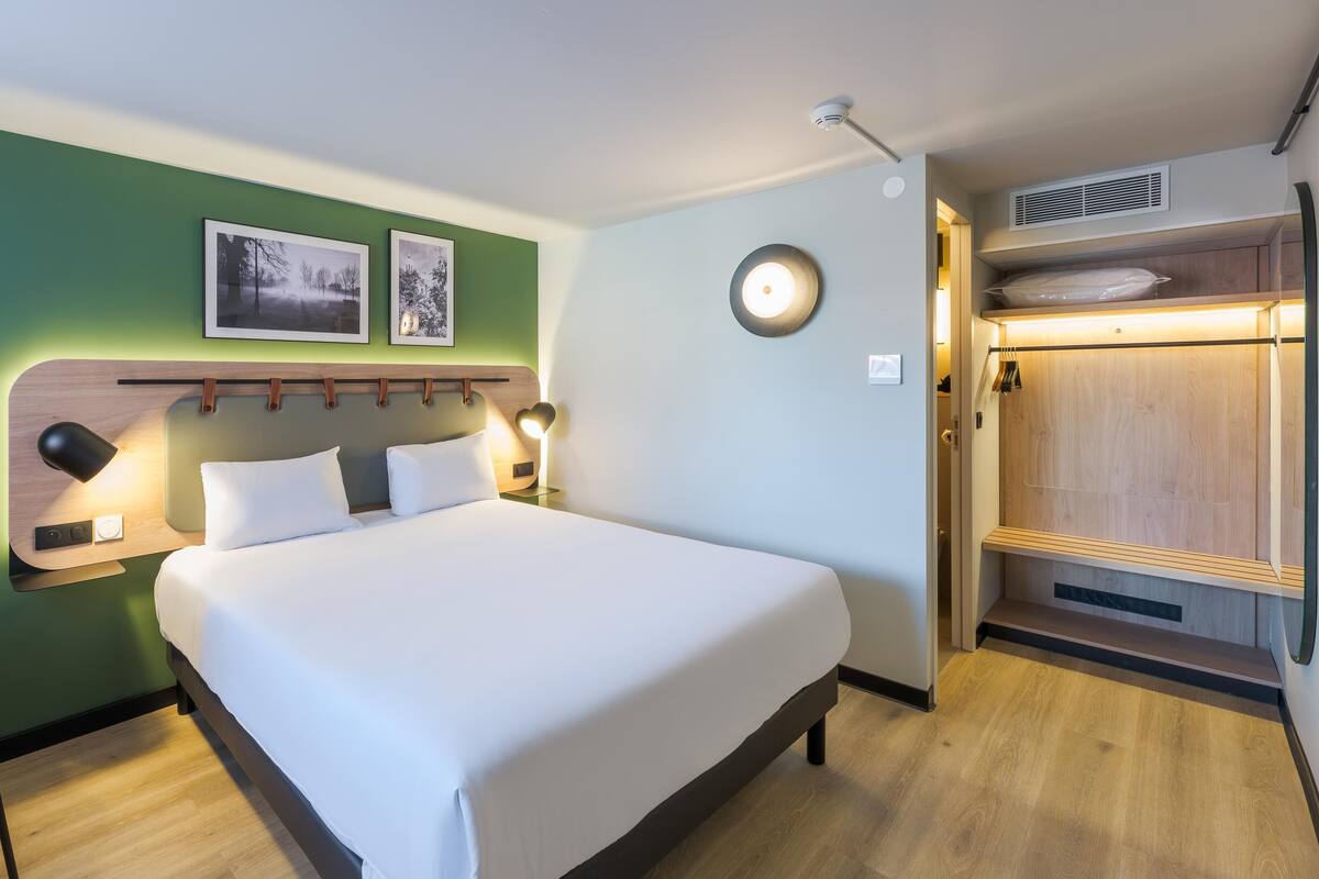 Een hotelkamer met een bed, nachtkastjes, een bureau en een stoel. Er is een kledingkast met een spiegel en een kledingroede.