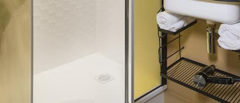 Un baño moderno con ducha de vidrio, un lavamanos blanco y una encimera negra, y un espejo sobre el lavamanos.