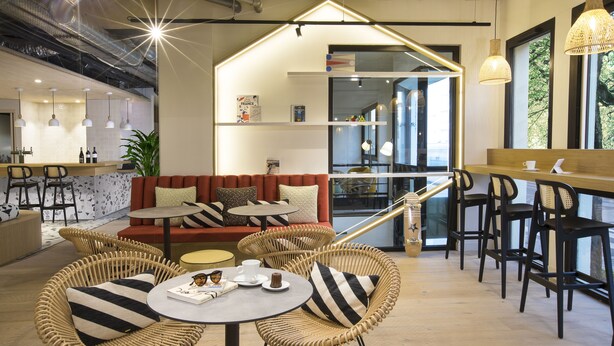 Un café moderne avec des meubles en osier, un coin bar et un espace salon comprenant un canapé et des tables.
