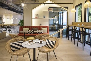 Un café moderne avec des meubles en osier, un coin bar et un espace salon comprenant un canapé et des tables.