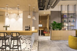 Un hall d’hôtel moderne doté d’un bar, de coins salon et d’un comptoir d’accueil.