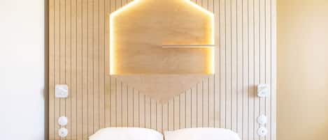 Et hotelværelse med væg af træpaneler, en seng med hvide sengetøj og en unik geometrisk lampe over sengen.