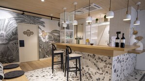 Un espace bar moderne avec un comptoir en bois, deux tabourets de bar et des luminaires suspendus.