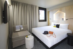 Une chambre d’hôtel avec un lit, un canapé, une petite table, une télévision et une fenêtre avec des rideaux.