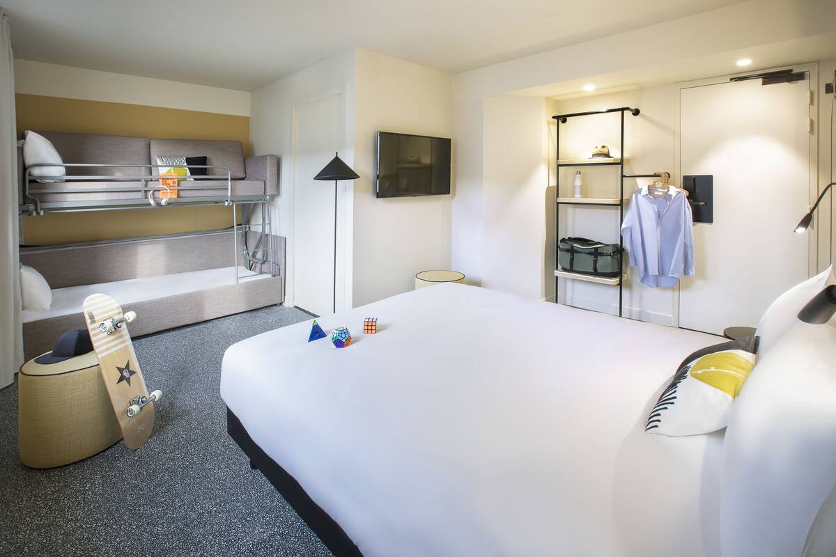 Ein Hotelzimmer mit einem Etagenbett, einem Flachbildfernseher, einem Schreibtisch mit Lampe und einem Kleiderschrank mit Kleidung.