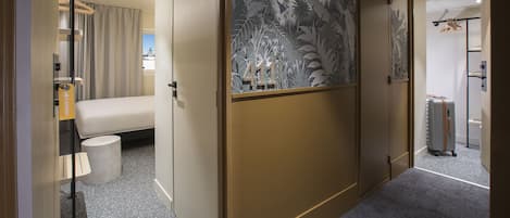 Una habitación de hotel con cama, una mesita, una silla, una maleta y un armario.