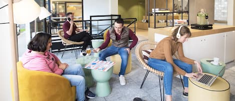 Un espacio moderno de *co-working* con zonas de estar, una estación de café y un mostrador visible con dispensador de bebidas.