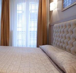 Una habitación de hotel con una cama grande, un cabecero de diseño ondulado y vistas a través de una ventana con cortinas.