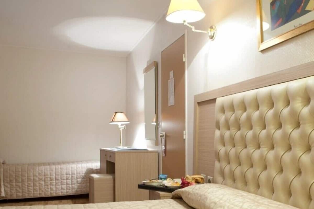 A hotel room with a large bed, a bedside table, a lamp, and a painting on the wall.