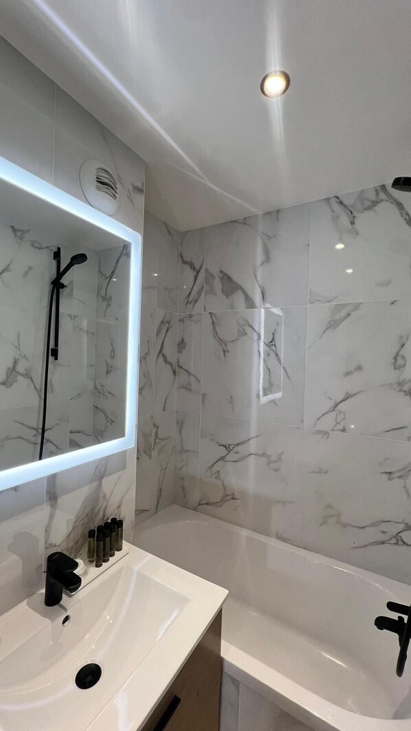A modern bathroom with a marble backsplash, a large mirror, a white sink, and a bathtub.