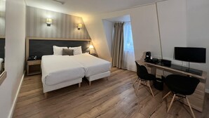 A hotel room with a double bed, a desk with a computer, a chair, and a TV. - Hôtel Lebron (Paris)