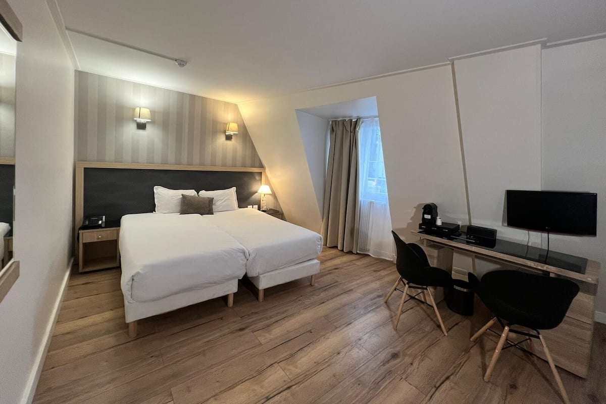 A hotel room with a double bed, a desk with a computer, a chair, and a TV.
