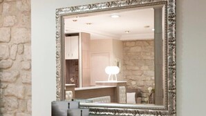 A mirror with an ornate frame, a wooden console table with decorative items, and a stone wall. - Hôtel Lebron (Paris)