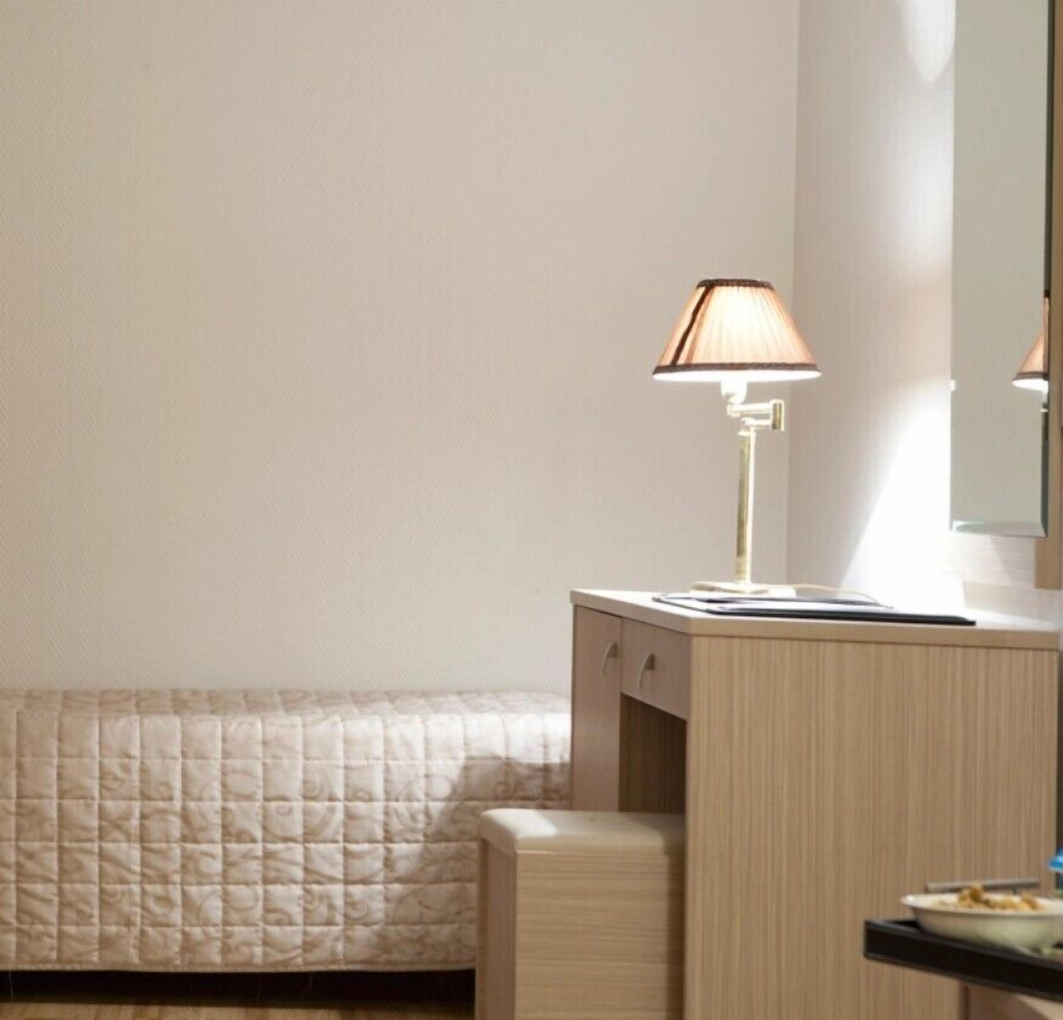 A bedroom with a bed, a bedside table, a lamp, and a mirror.