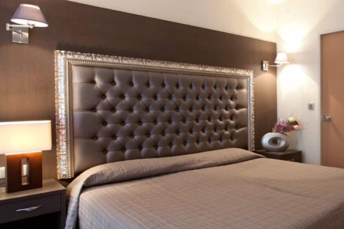 A bedroom with a tufted headboard, a bedside table with a lamp, and a nightstand with a vase of flowers.