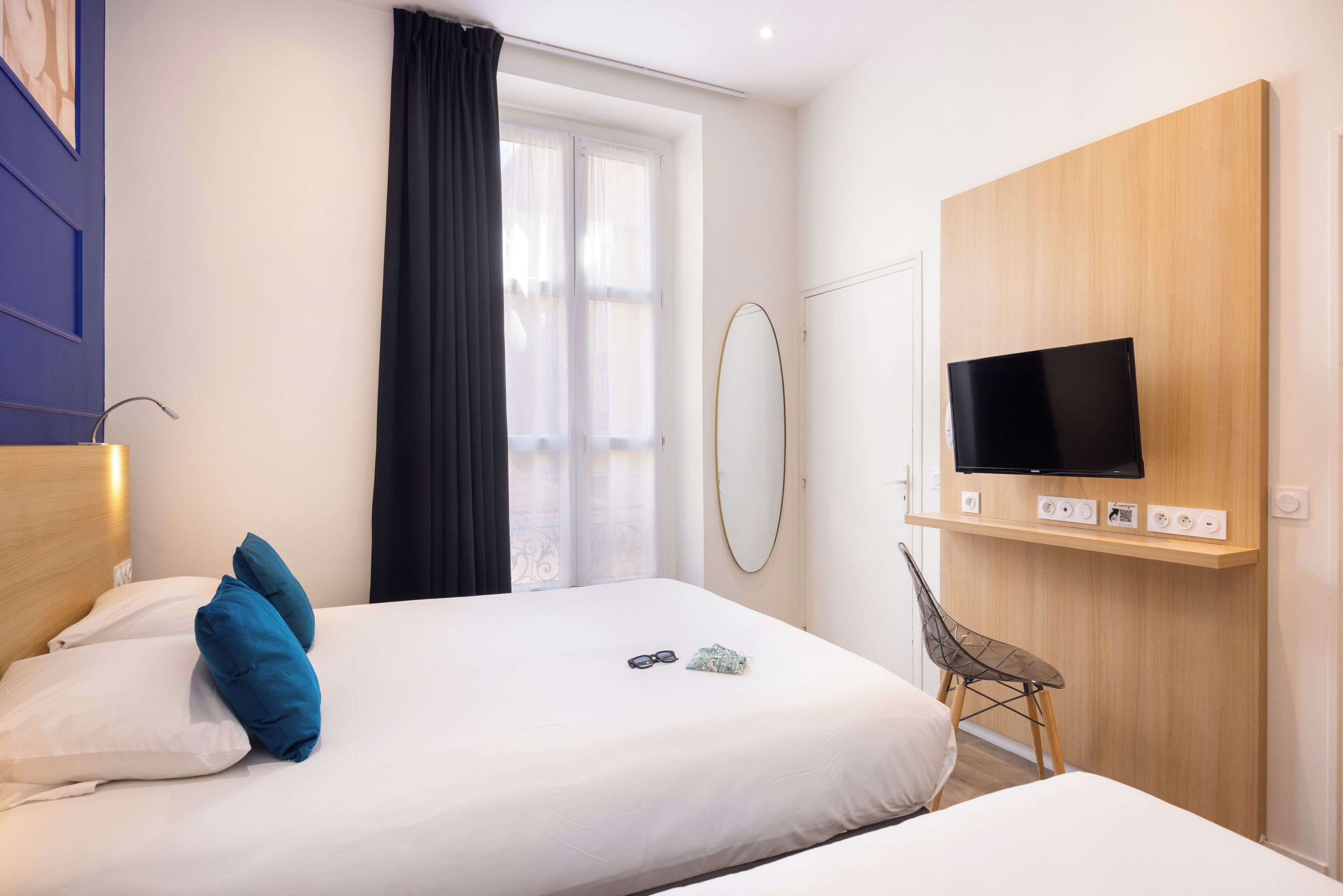 A hotel room with a bed, a TV, a chair, and a window with curtains.
