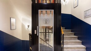 Un ascenseur moderne doté d’une porte en verre et d’un logo, situé à côté d’un escalier dont les murs sont peints en bleu et en blanc.