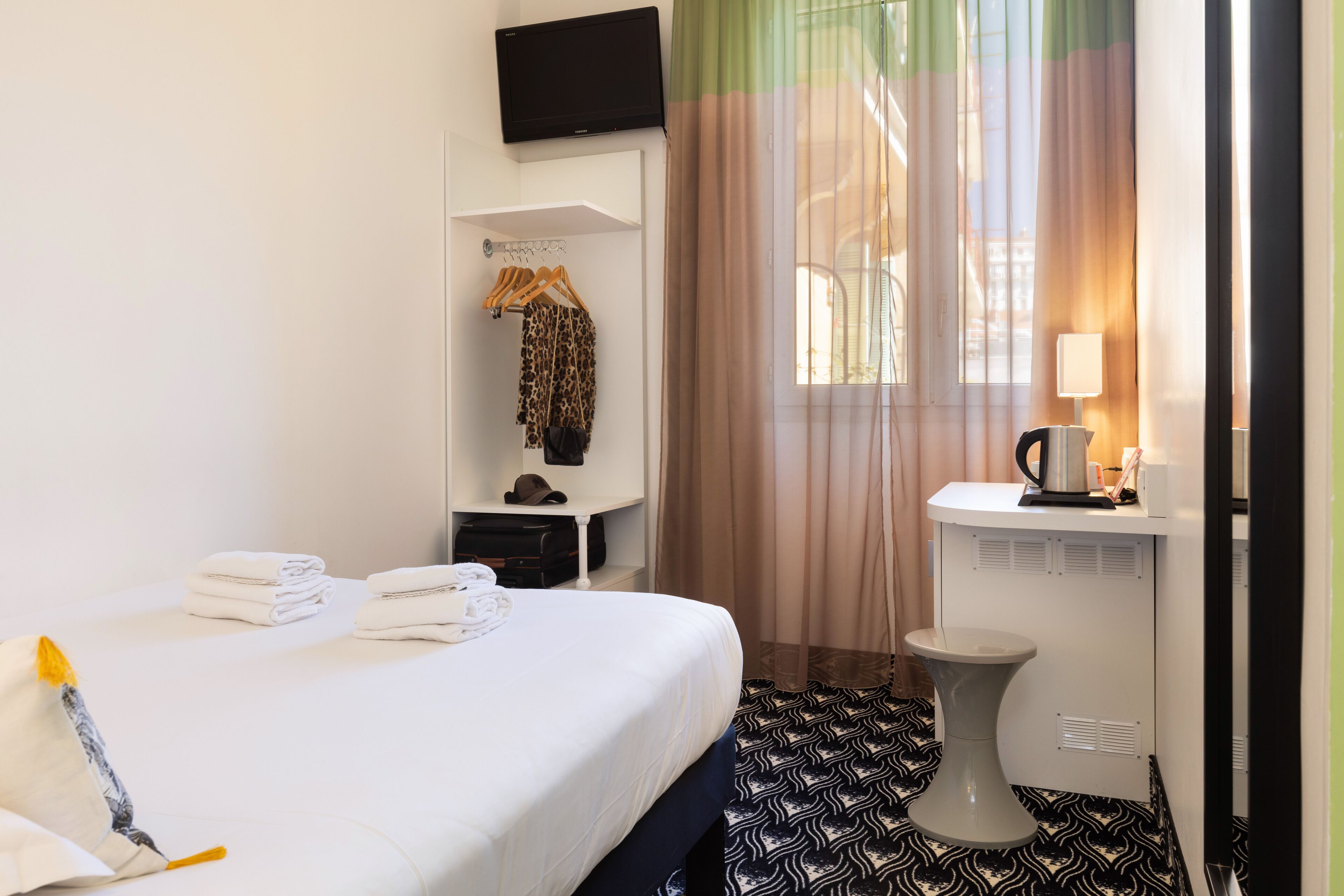 Une chambre d’hôtel avec un lit, une armoire, un bureau avec une lampe et un téléviseur fixé au mur.