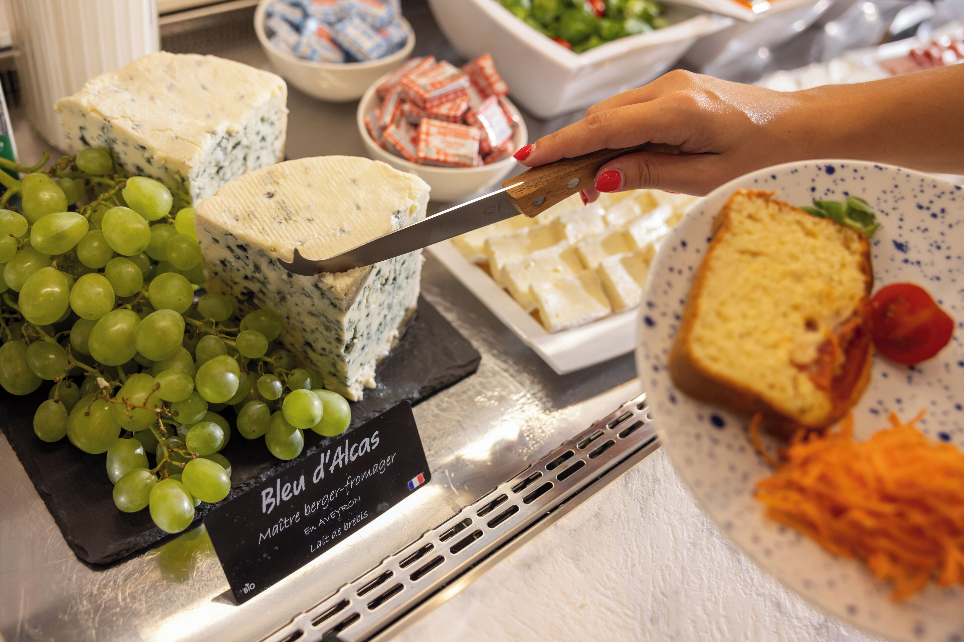 Una tabla de quesos con diferentes tipos de queso, uvas y un letrero que indica Bleu d'Alcas.