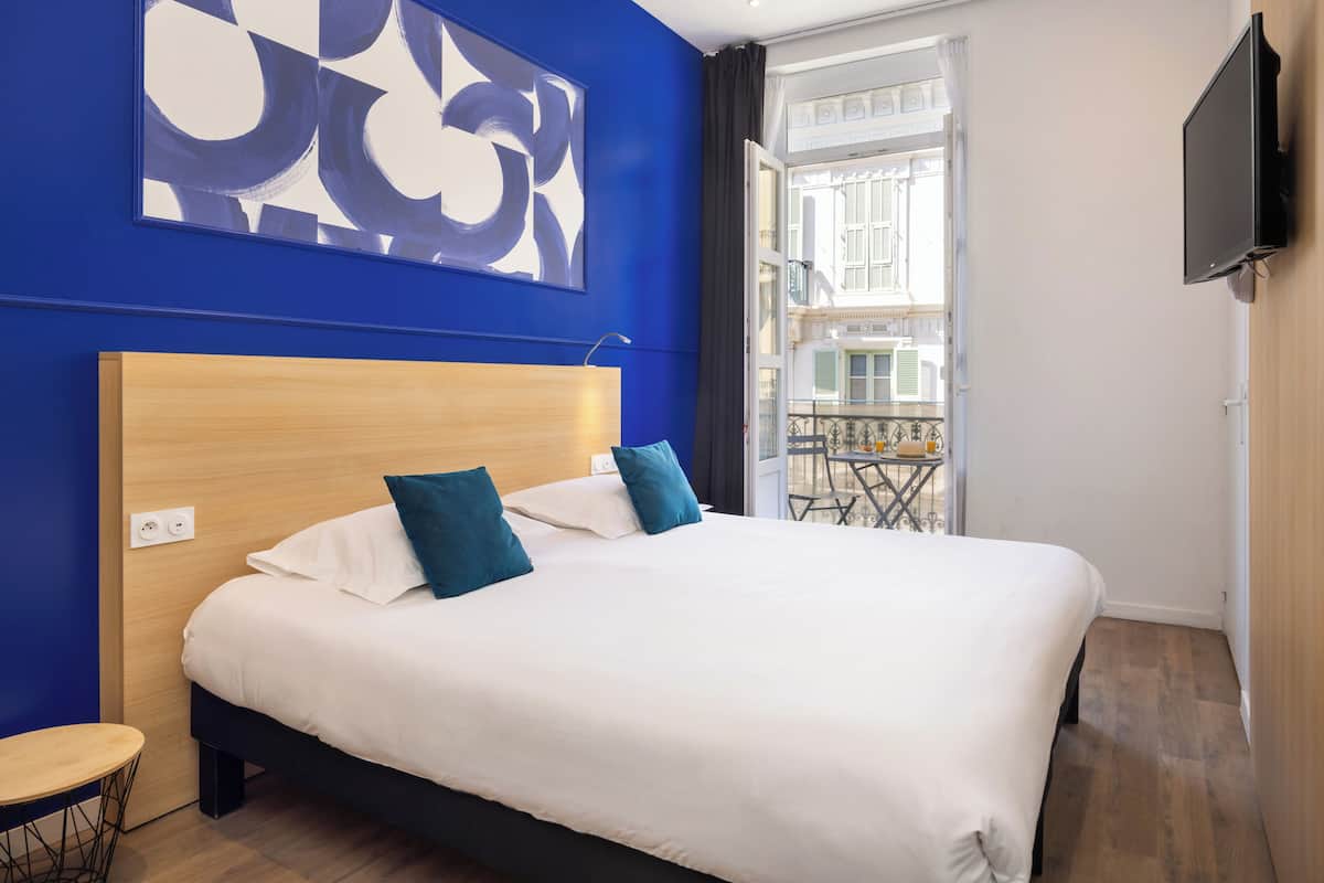 Une chambre d’hôtel avec un grand lit, une vue sur l’extérieur, un téléviseur fixé au mur et une petite table près de la fenêtre.