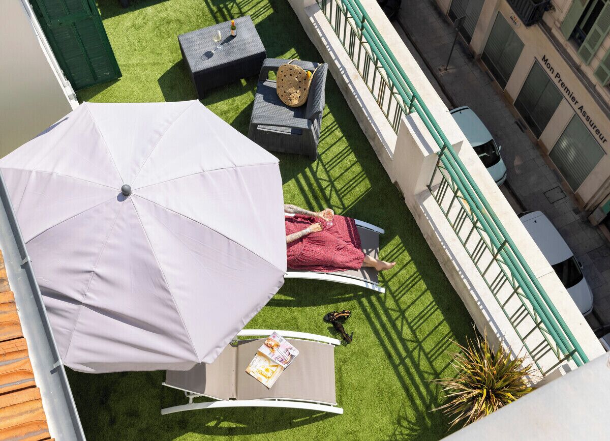 Une terrasse sur le toit, avec un parasol blanc, un fauteuil de relaxation et une petite table sur laquelle est posé un magazine.