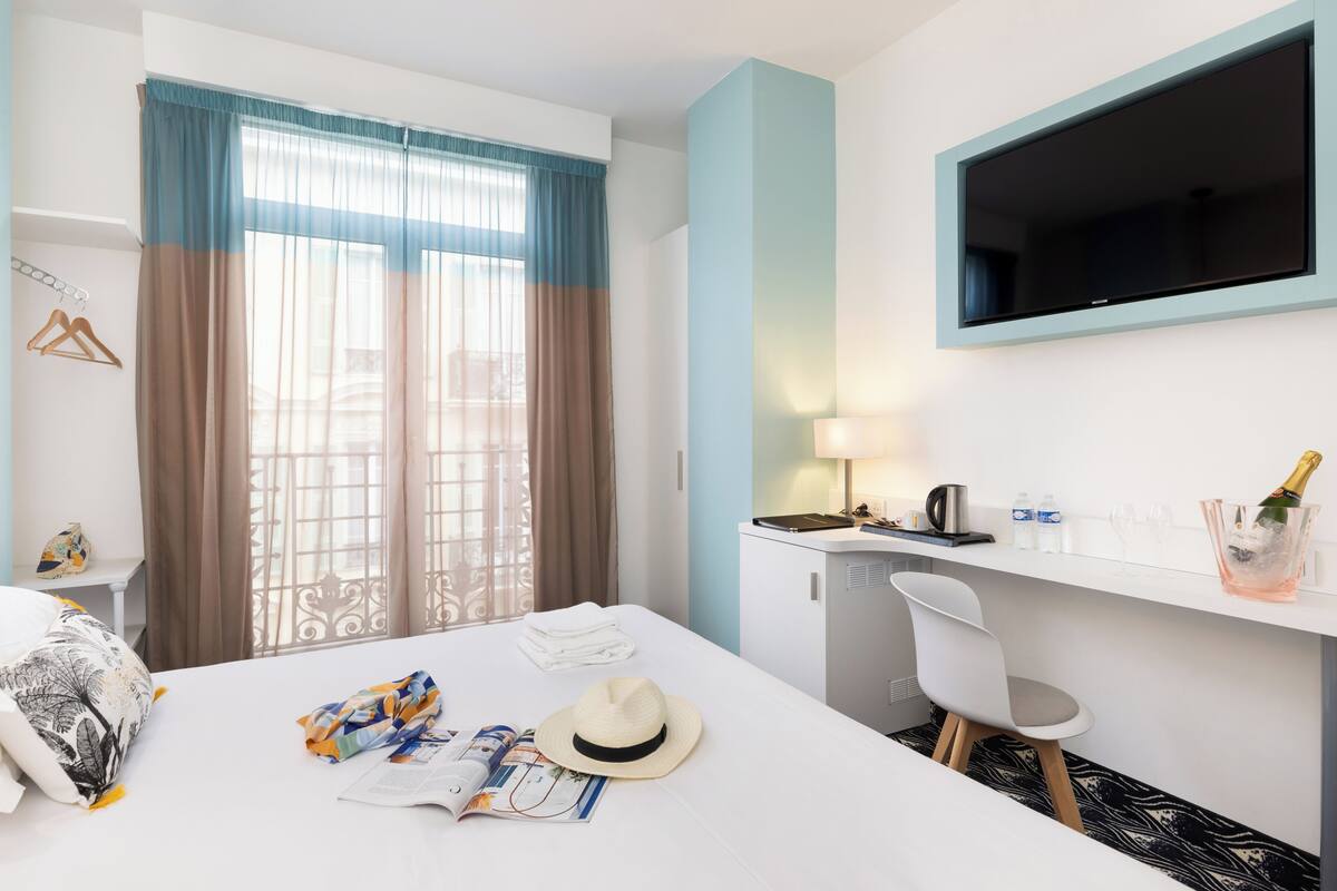 Une chambre d’hôtel équipée d’un lit, d’un bureau avec un ordinateur, d’une télévision, d’une chaise et d’un mini-bar.