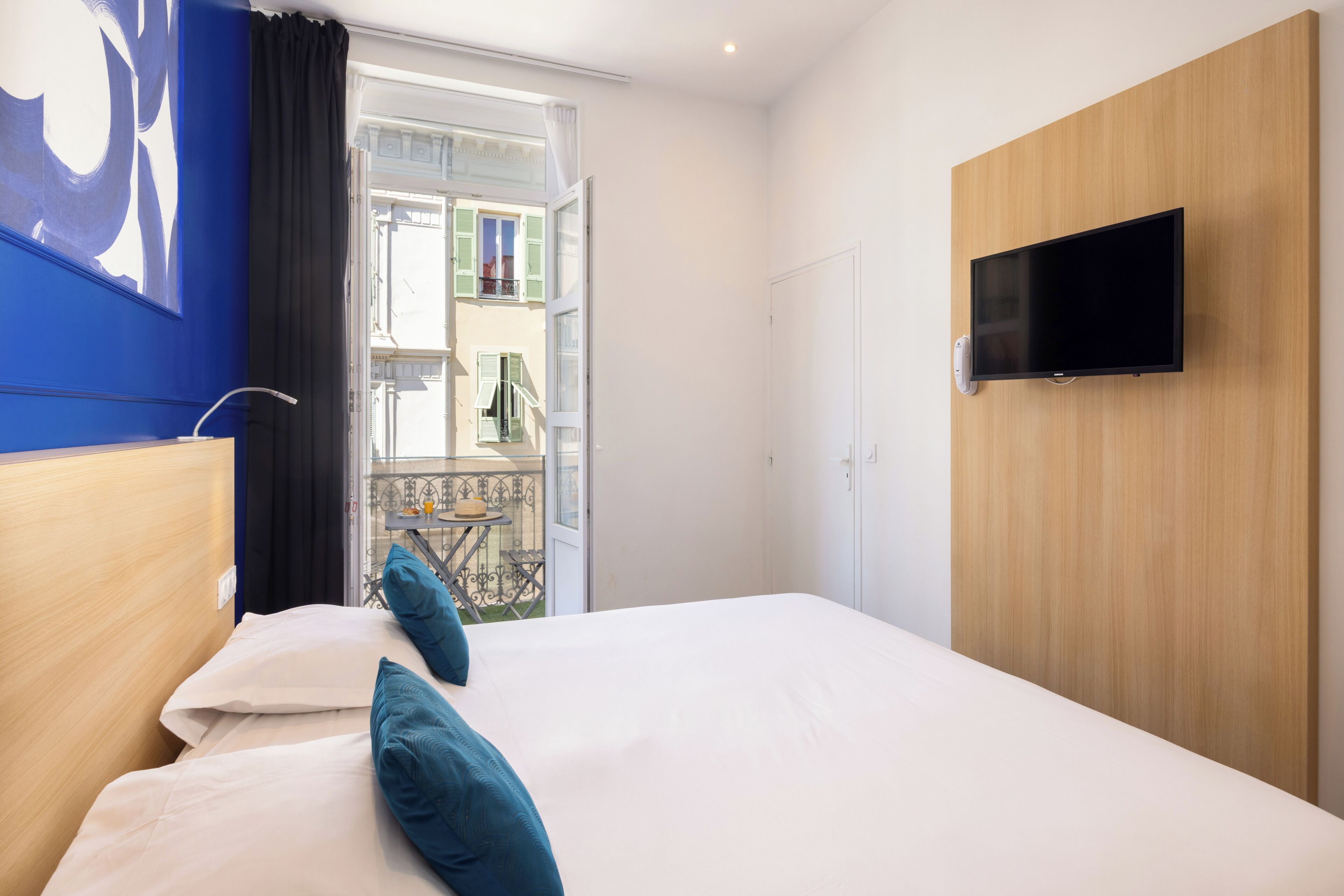 A hotel room with a bed, a TV mounted on the wall, and a balcony with a table and chairs.