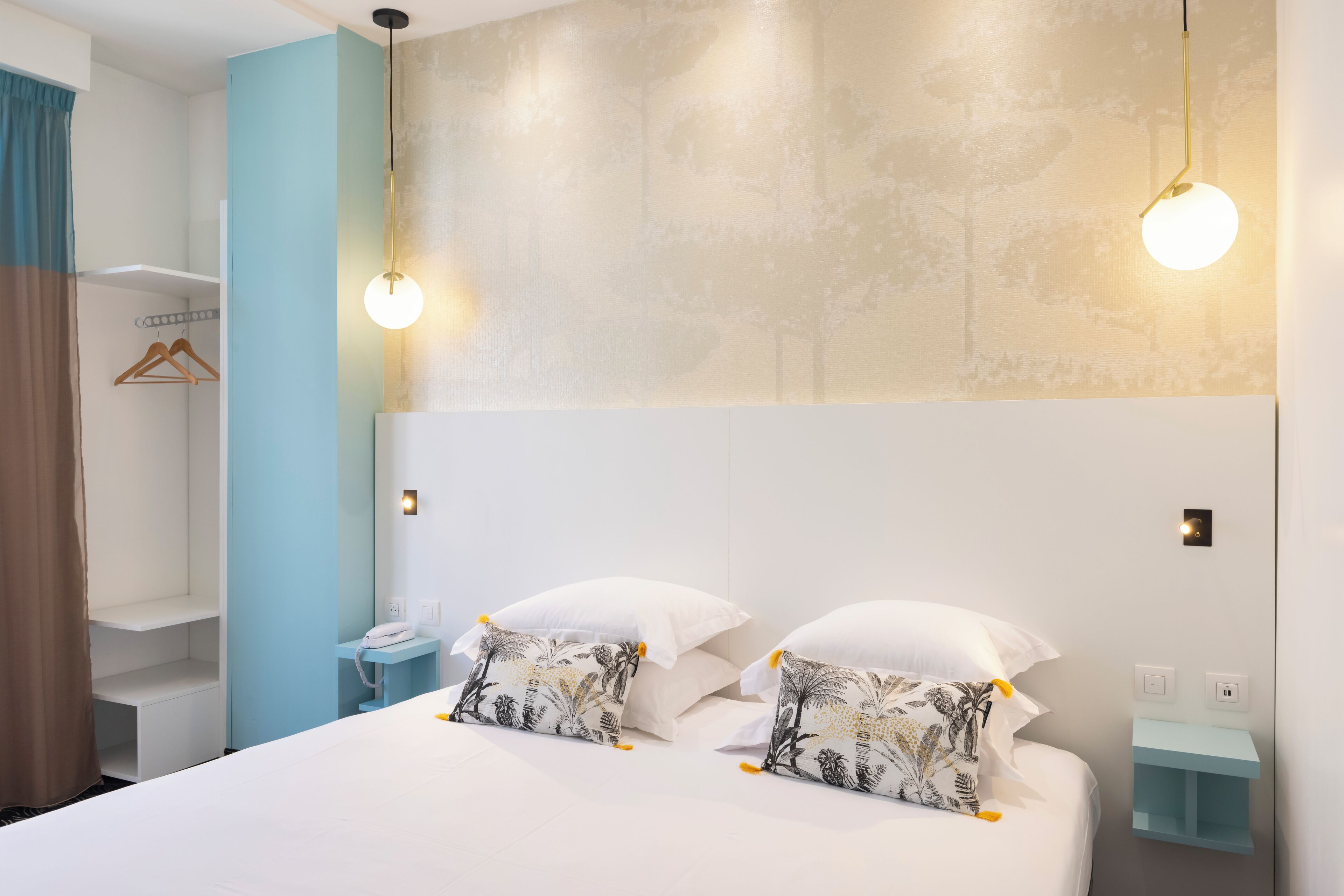 Una camera d'albergo con un letto, un comodino, una lampada a sospensione e un armadio.