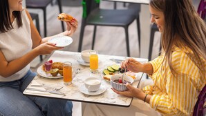 Deux personnes sont assises à une table, devant un petit-déjeuner composé de pain grillé, de fruits et d’une boisson.