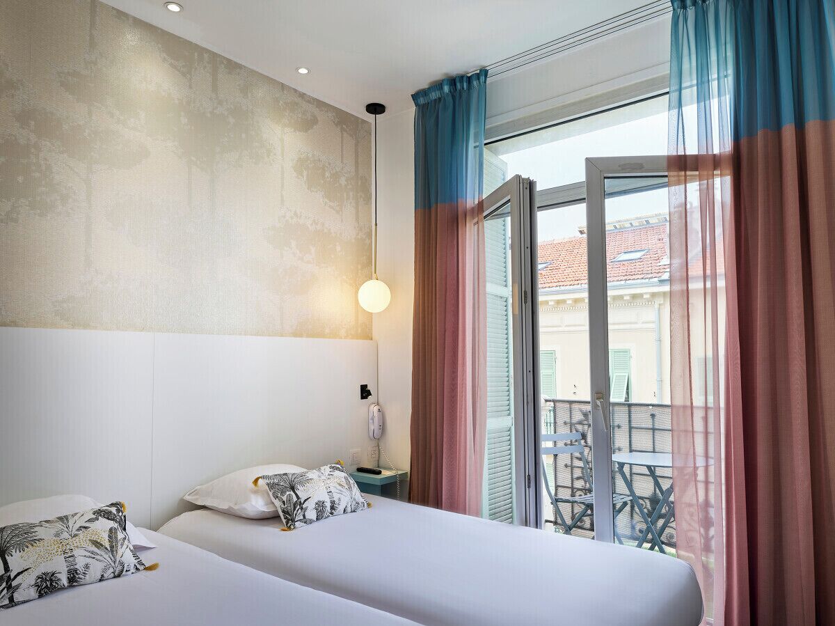 A hotel room with a bed, bedside table, and a view of the outside balcony.