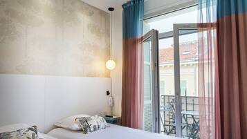 A hotel room with a bed, bedside table, and a view of the outside balcony.