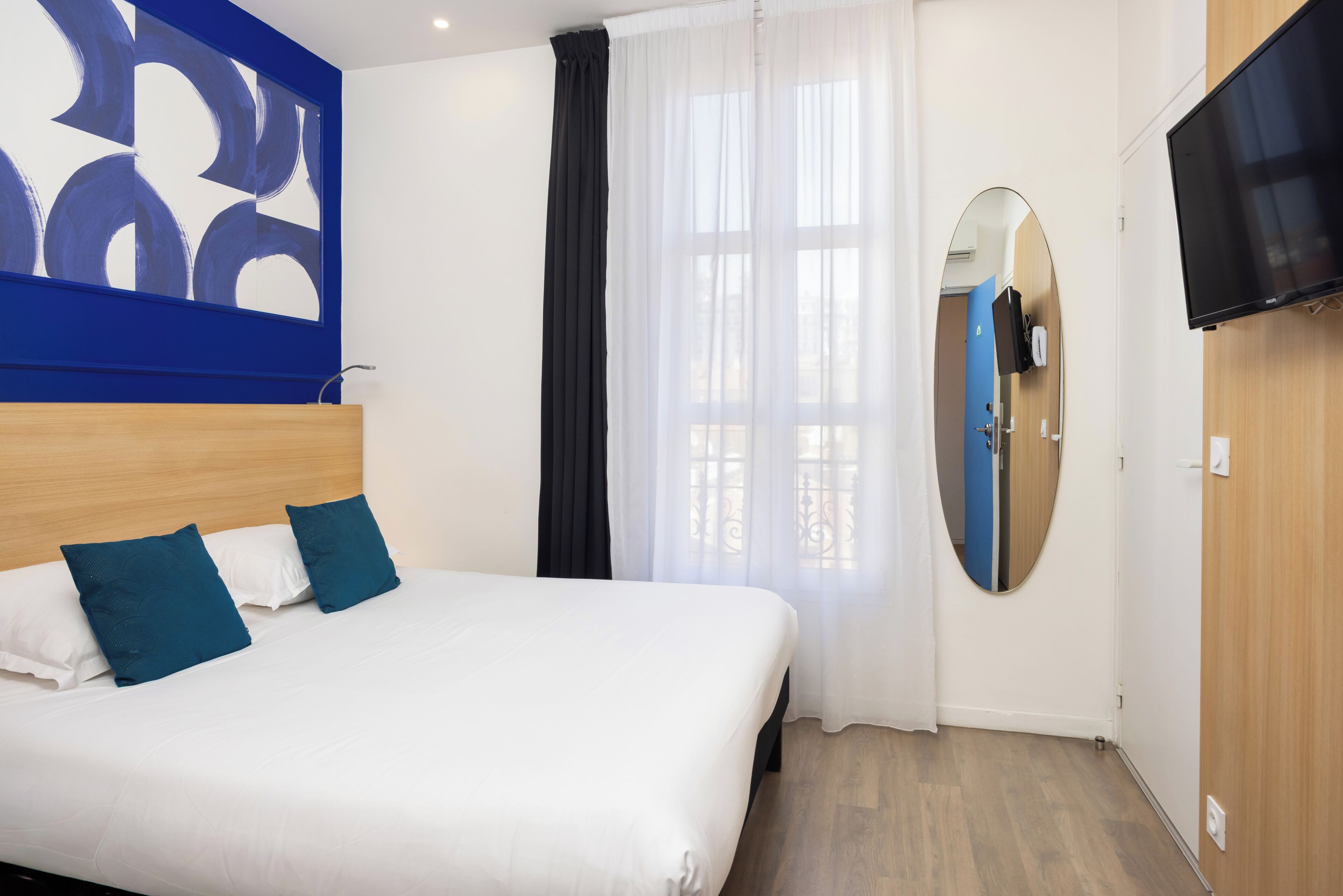 Ett hotellrum med en stor säng, en tv som är monterad på väggen och en spegel på dörren.