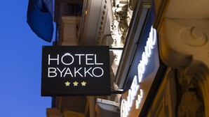 Une enseigne d’hôtel ornée de drapeaux, dont le drapeau de l’Union européenne et un drapeau national, et portant le nom « HÔTEL BYAKKO ».
