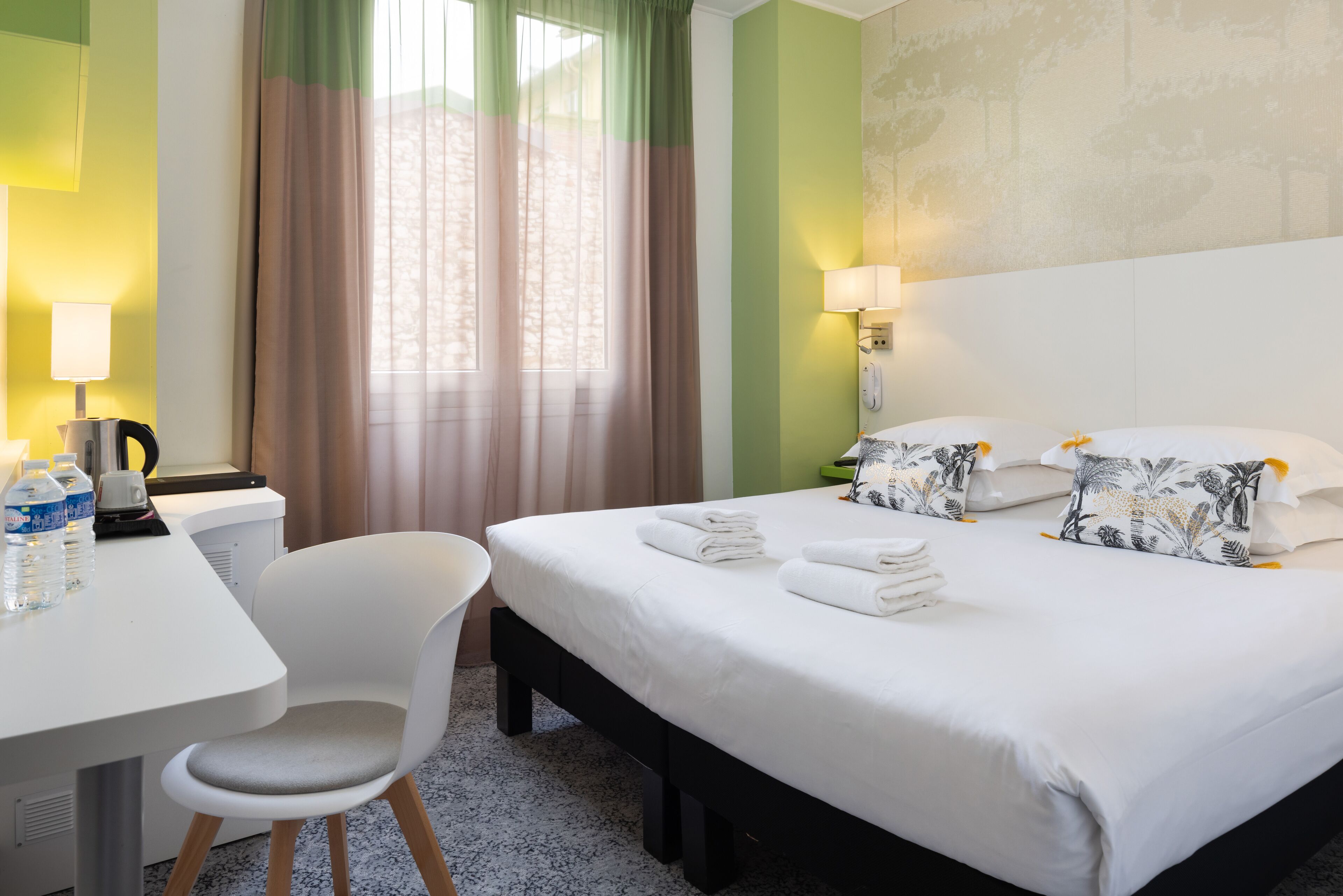 Une chambre d’hôtel comprenant un lit, un bureau avec une chaise, une lampe et un téléphone.