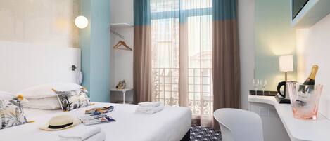 A hotel room with a bed, a desk with a chair, a window with curtains, a TV, and a minibar.