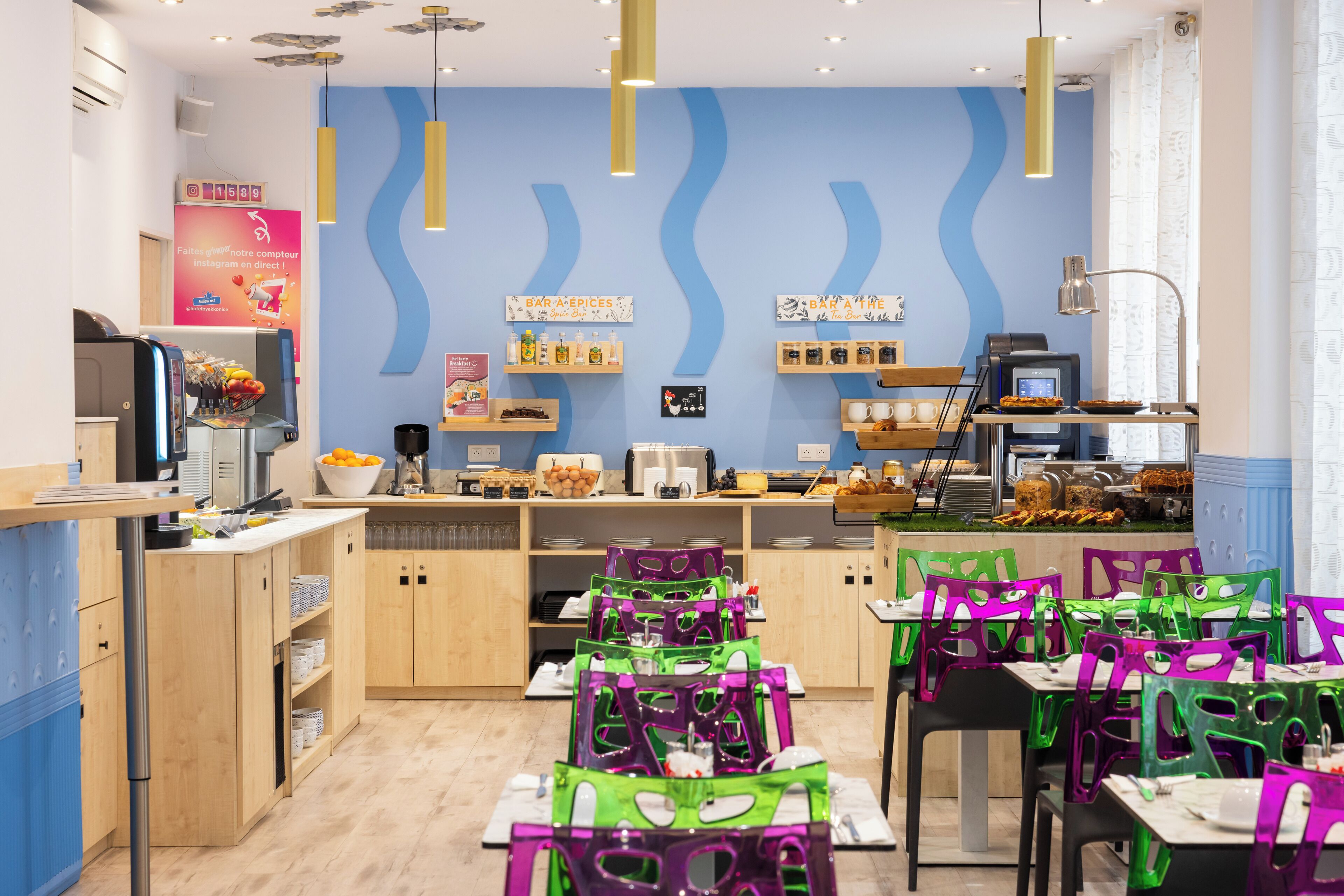 A restaurant with a modern interior, featuring wooden cabinets, a counter with a display of food items, and green and purple chairs.