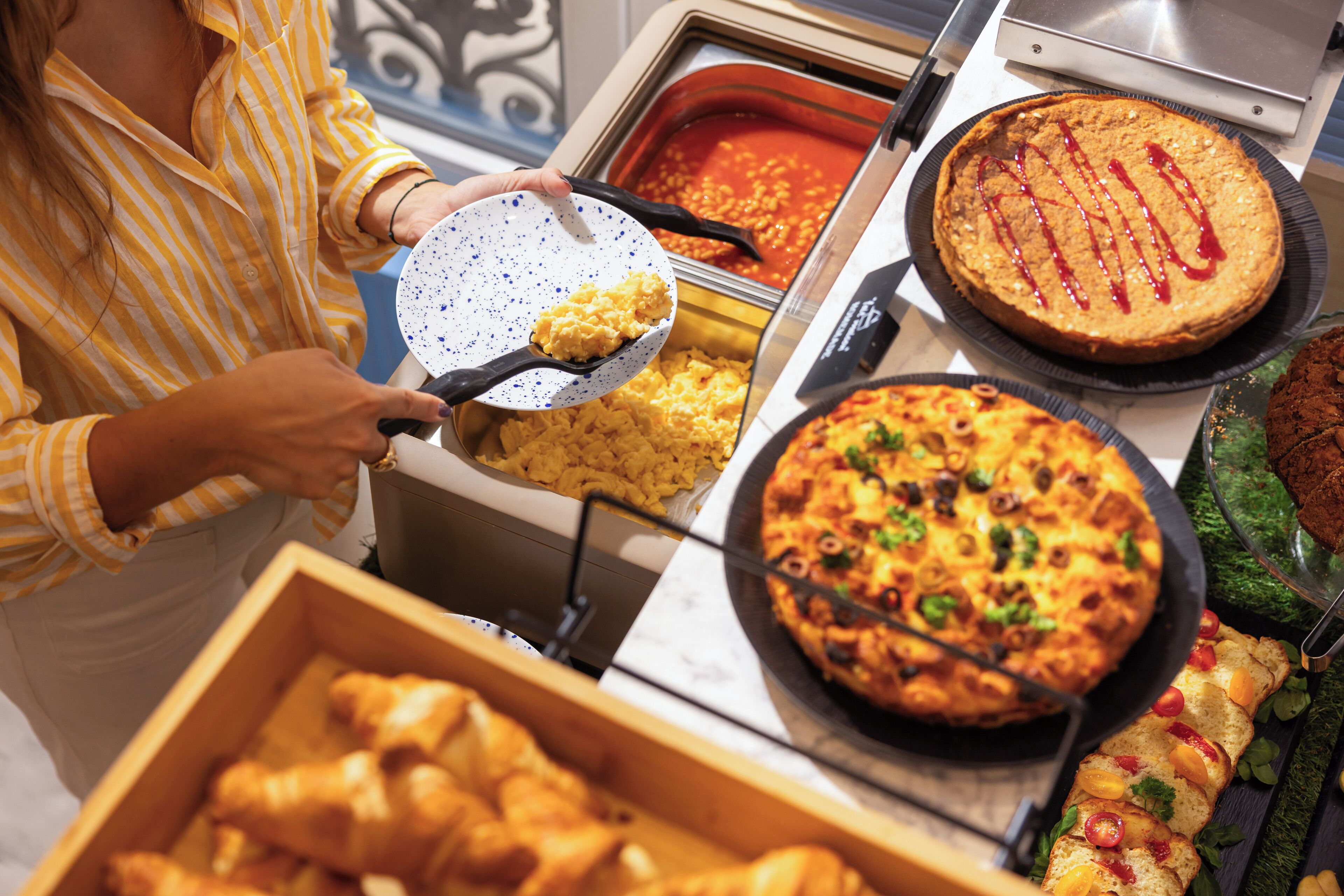 Un buffet proposant divers plats, notamment des œufs brouillés, une tarte et une pizza.