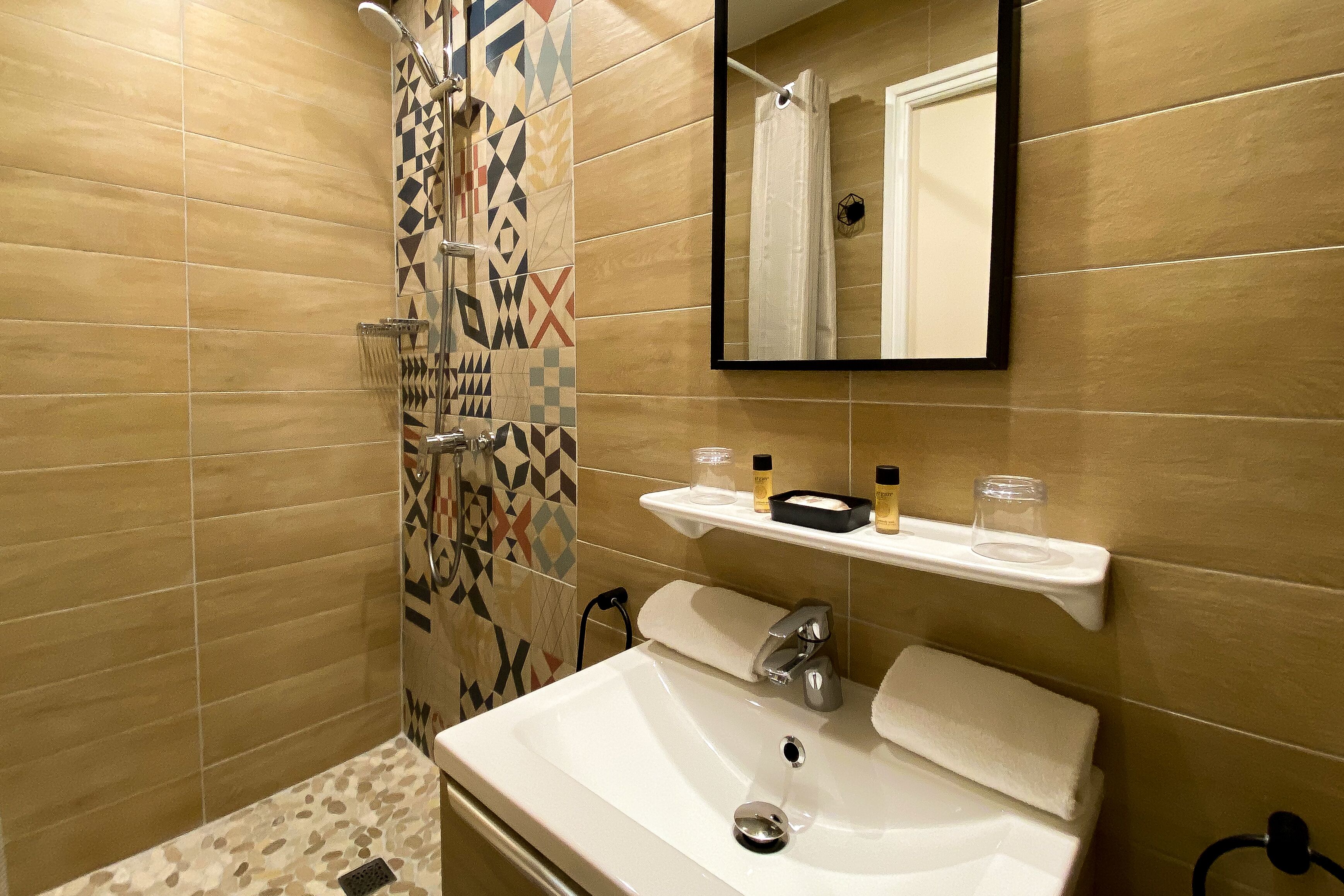 A bathroom with a shower, a sink, a mirror, and a shelf with toiletries.