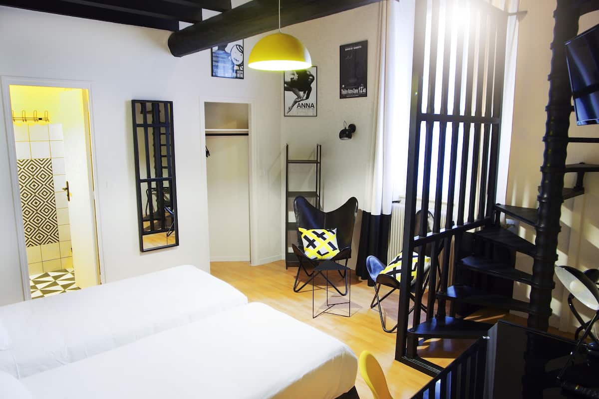 Habitación de hotel con cama, escritorio, silla, escalera y una lámpara colgante amarilla.