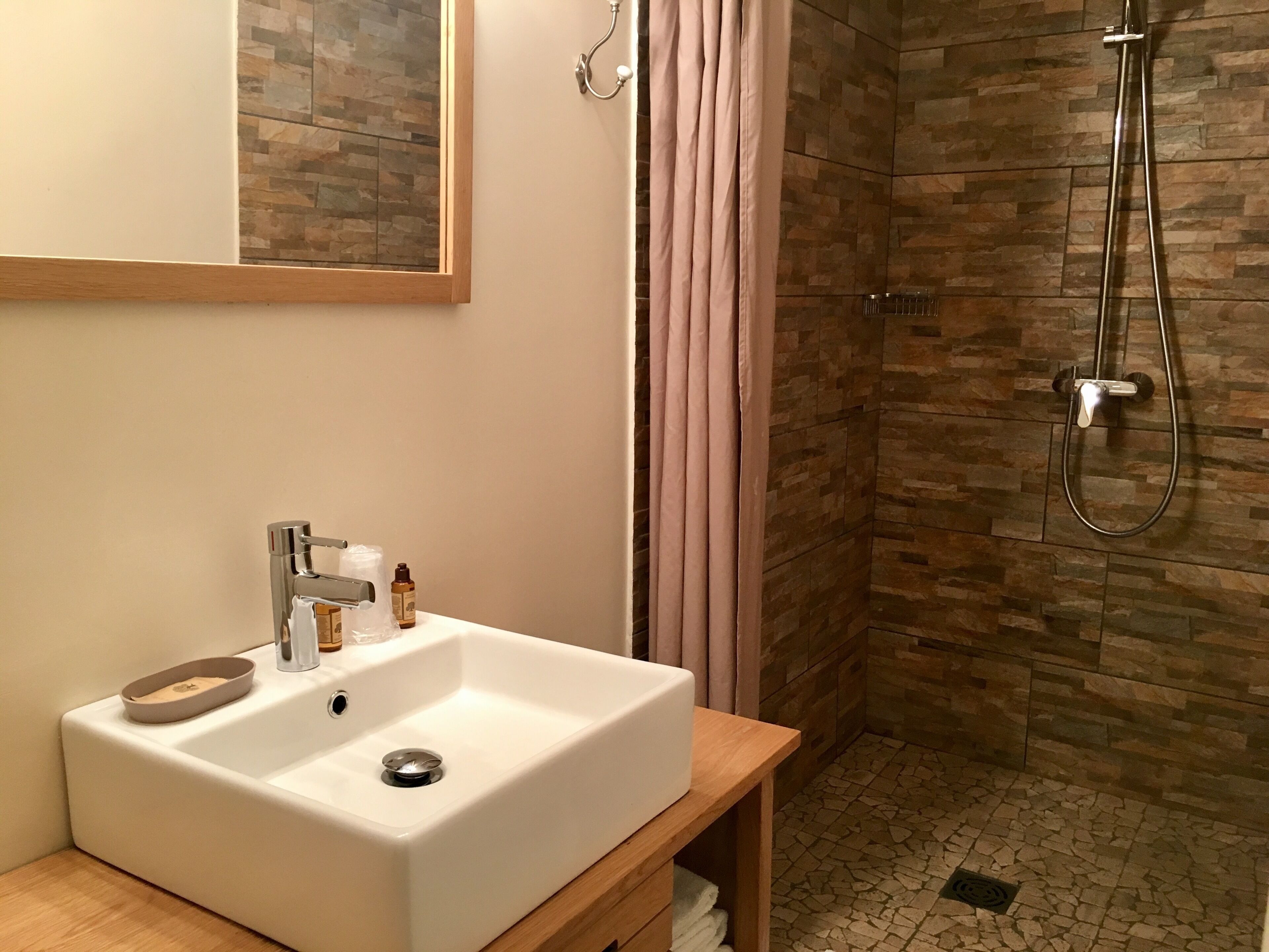 A bathroom with a white sink, a mirror, a shower with a glass door, and a stone-patterned wall.