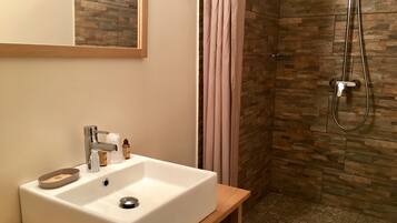 A bathroom with a white sink, a mirror, a shower with a glass door, and a stone-patterned wall.