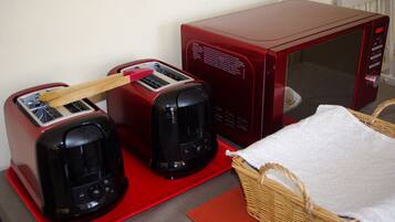 Una kitchenette con un tostador rojo, un microondas rojo y una cesta de mimbre sobre un tapete rojo.