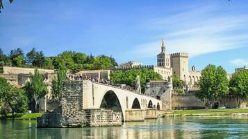Un puente de piedra con arcos que cruza un río, conduciendo a un castillo histórico con una torre destacada.