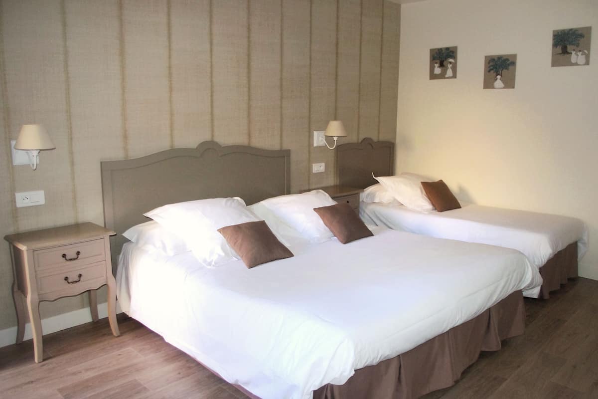 Habitación de hotel con dos camas, una mesita de noche con cajones, lámparas de pared y tres cuadros enmarcados.
