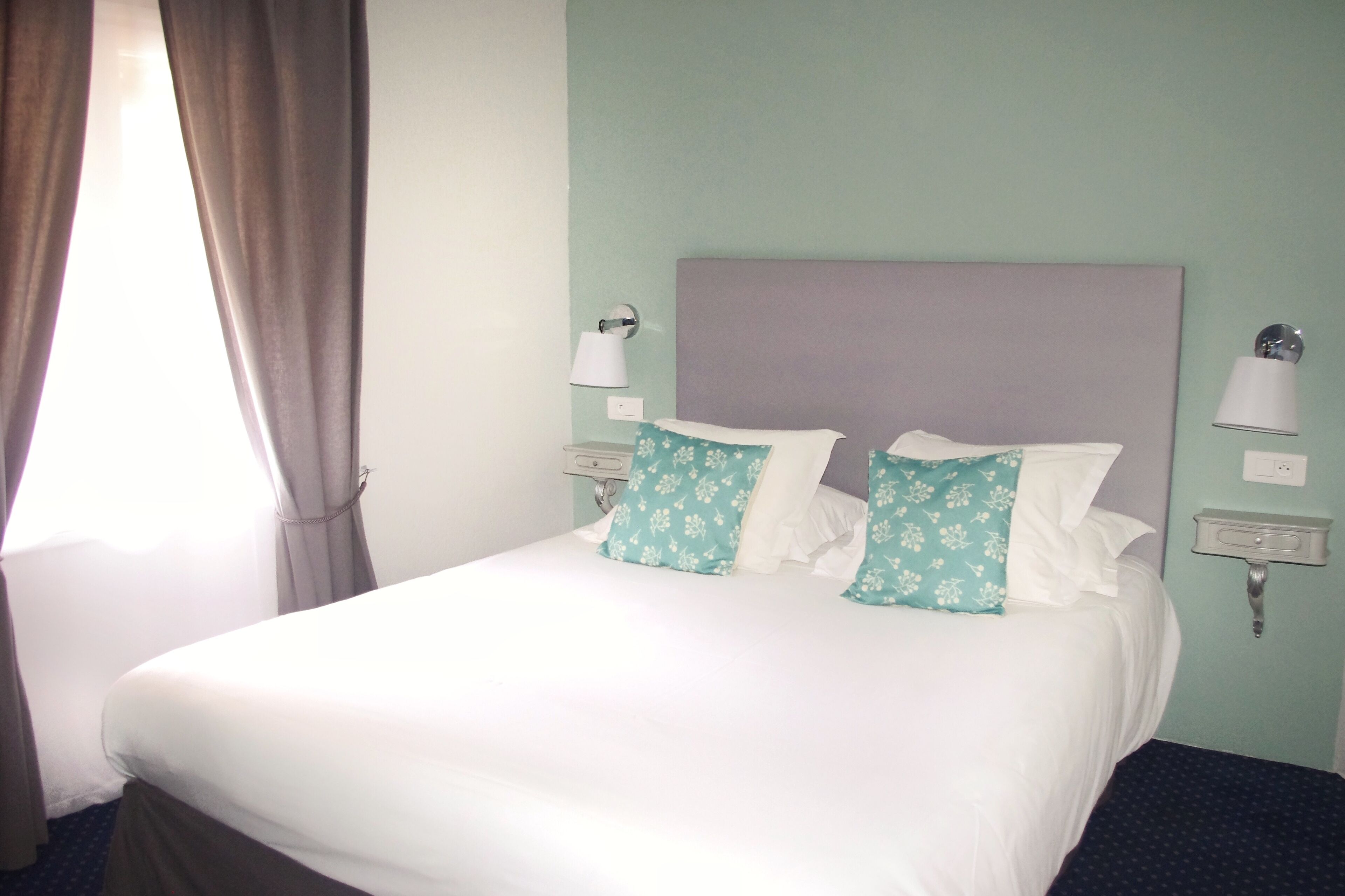 Habitación de hotel con una cama, dos almohadas, una mesita de noche, una lámpara y un enchufe de pared.