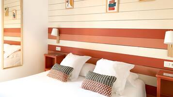 A hotel room with a bed, two bedside tables, a nightstand, a mirror, and a wall with framed artwork.