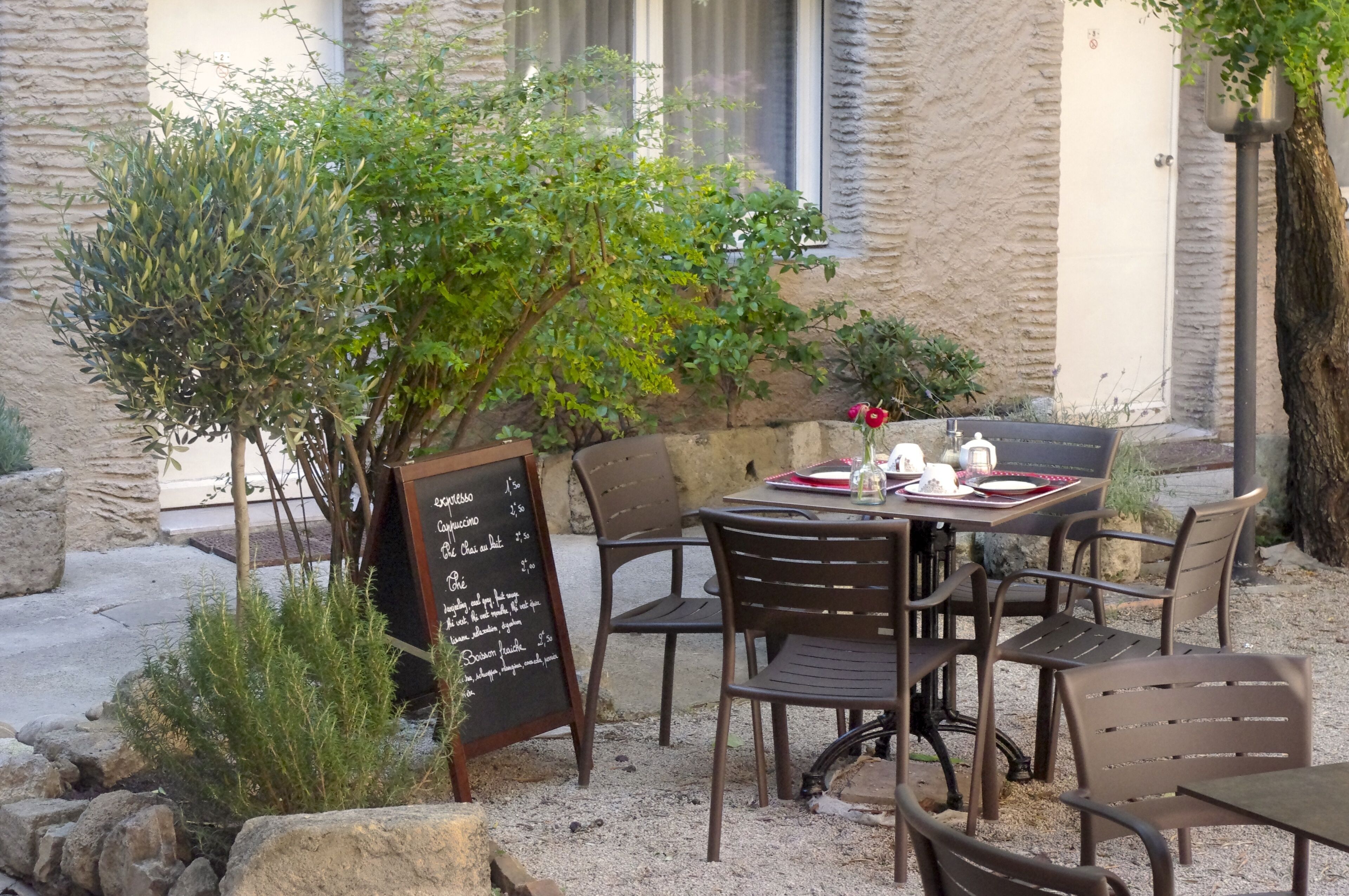 An outdoor seating area with a table and chairs, a chalkboard menu, and a small tree.