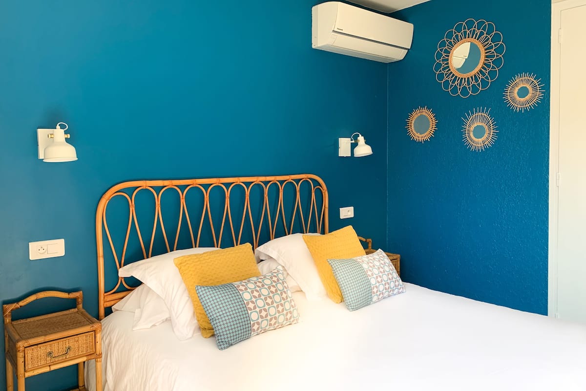 Un dormitorio con una pared azul, un cabecero de madera y una colcha blanca.